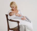 Woman breastfeeding a baby in a chair with a plain background