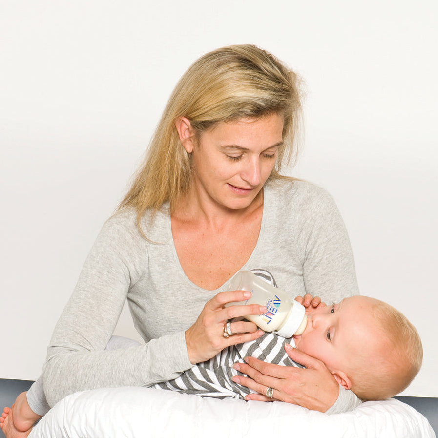 mother sitting on the floor with a baby using a white feeding pillow