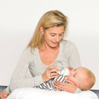 mother sitting on the floor with a baby using a white feeding pillow