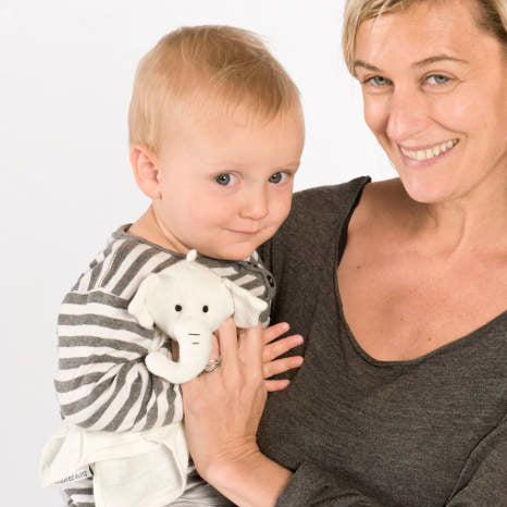Woman holding a baby with a white my luvvie elephant comforter against a plain background