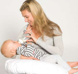 Woman holding a baby and feeding them with a bottle using the support of the inspired mother feeding and support pillow