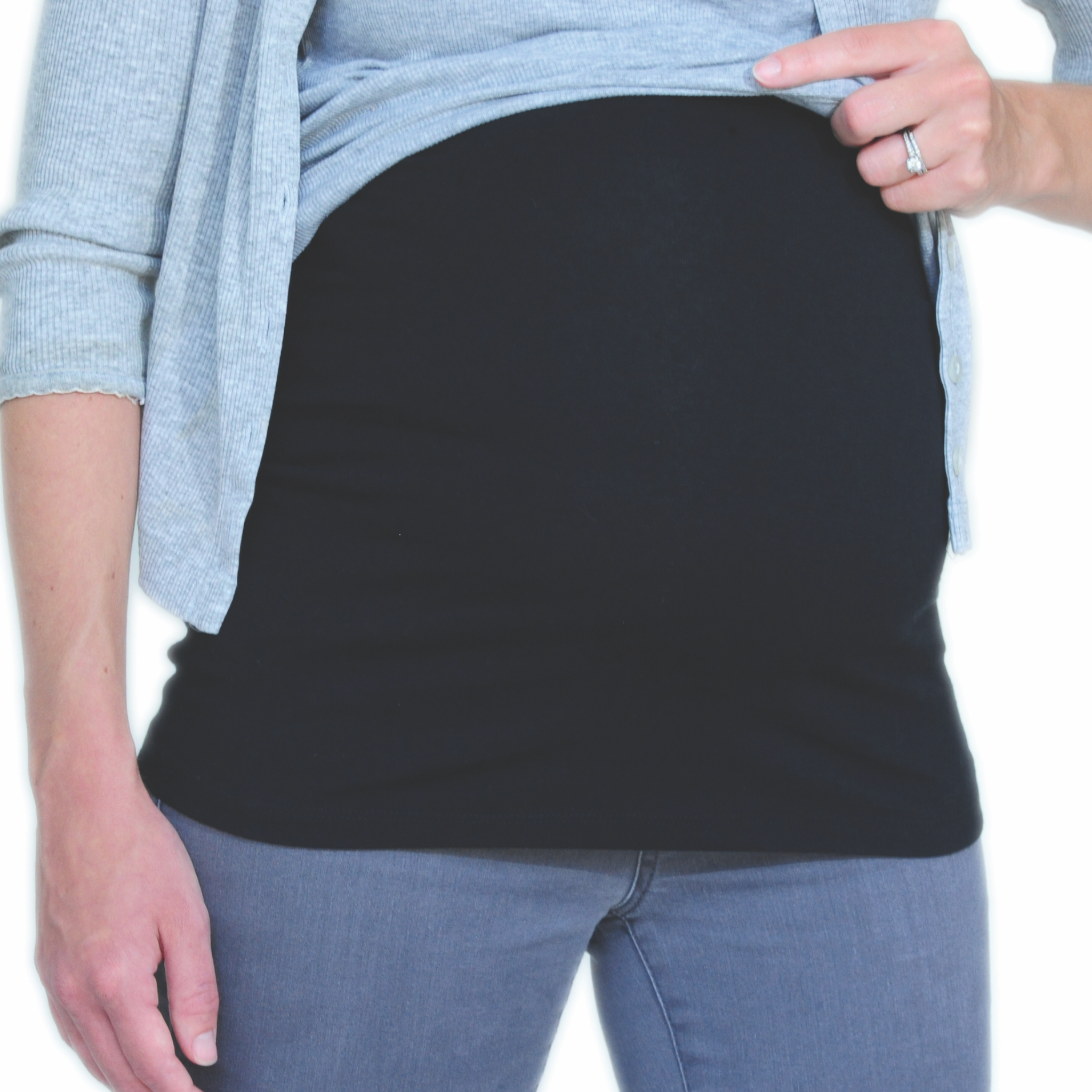 A close-up of a pregnant person wearing a black maternity tummy band over a light blue top and jeans, with one hand lifting the shirt to show the band around the belly.